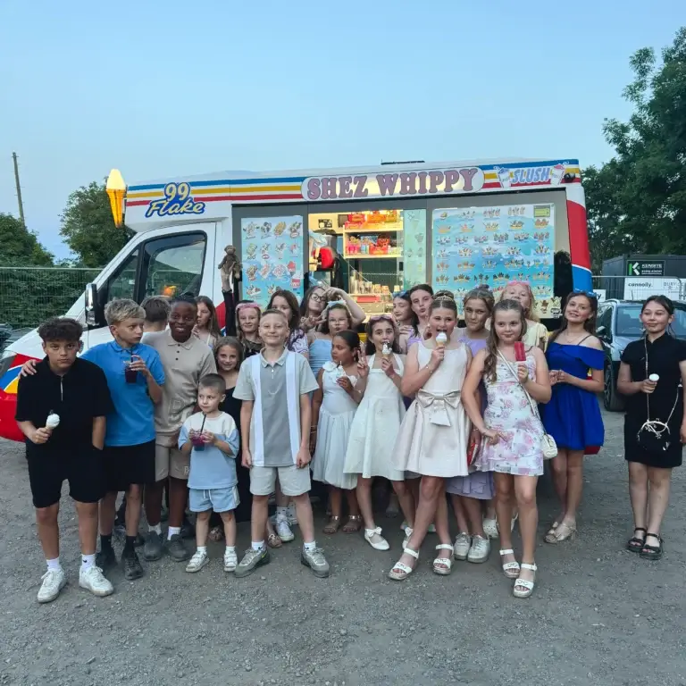 Shez Whippy, Ice Cream van for events. A group of schoolchildren and adults pose together outside a colourful Shez Whippy ice cream truck at a school event, with several children holding ice creams.