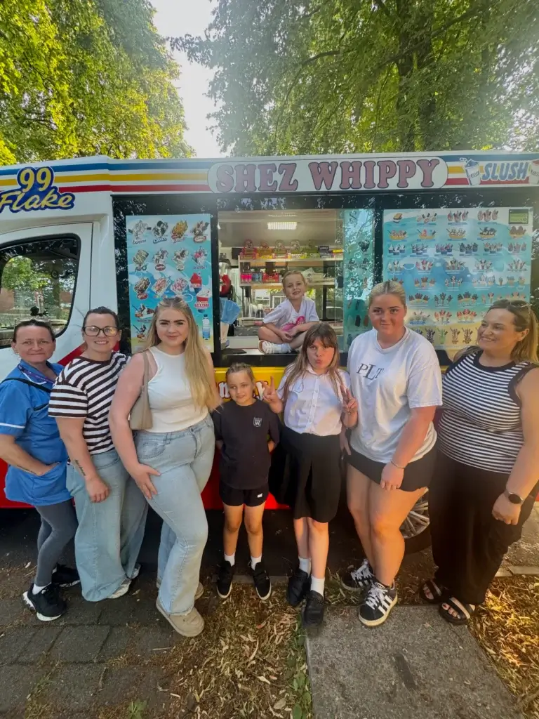 Shez Whippy, Ice Cream van for events. A group of adults and children pose in front of a Shez Whippy ice cream truck at a private event, with the truck’s ice cream and slush menu visible behind them.