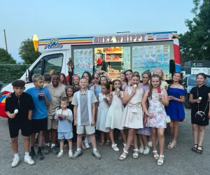 Shez Whippy, Ice Cream van for events. A group of schoolchildren and adults pose together outside a colourful Shez Whippy ice cream truck at a school event, with several children holding ice creams.